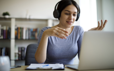 A woman with headphones is having a video call on her laptop.
